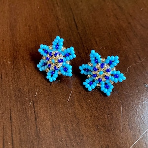 May include: A pair of blue and gold star-shaped earrings with a beaded design.