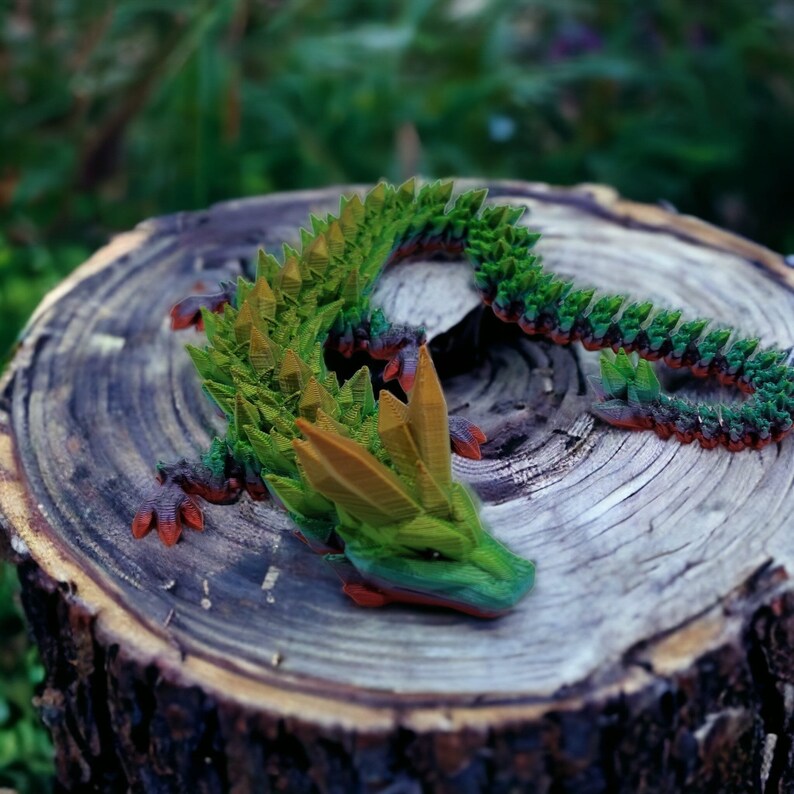May include: A green and orange origami dragon sculpture on a wooden stump. The dragon is made of paper and has a detailed design.
