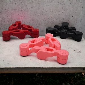 Op de afbeelding: Drie in elkaar grijpende kunststof onderdelen in rood, zwart en roze. De onderdelen zijn driehoekig gevormd en hebben aan de uiteinden een afgeronde, cilindrische vorm.