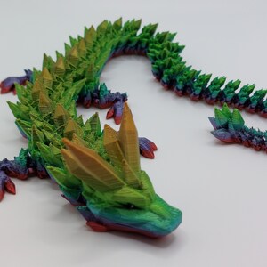 May include: A 3D printed dragon figurine with a green, yellow, and purple iridescent finish. The dragon has a long, spiky tail and a detailed head with a pointed snout.