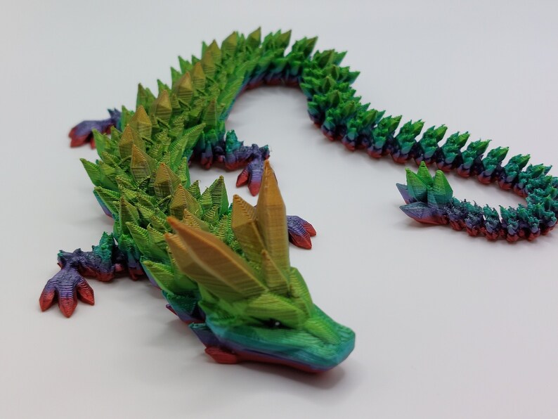 May include: A 3D printed dragon figurine with a green, yellow, and purple iridescent finish. The dragon has a long, spiky tail and a detailed head with a pointed snout.