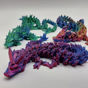 May include: Four 3D printed lizards in different iridescent colors: green, blue, red, and orange. The lizards are posed in a crawling position with their tails curled up.