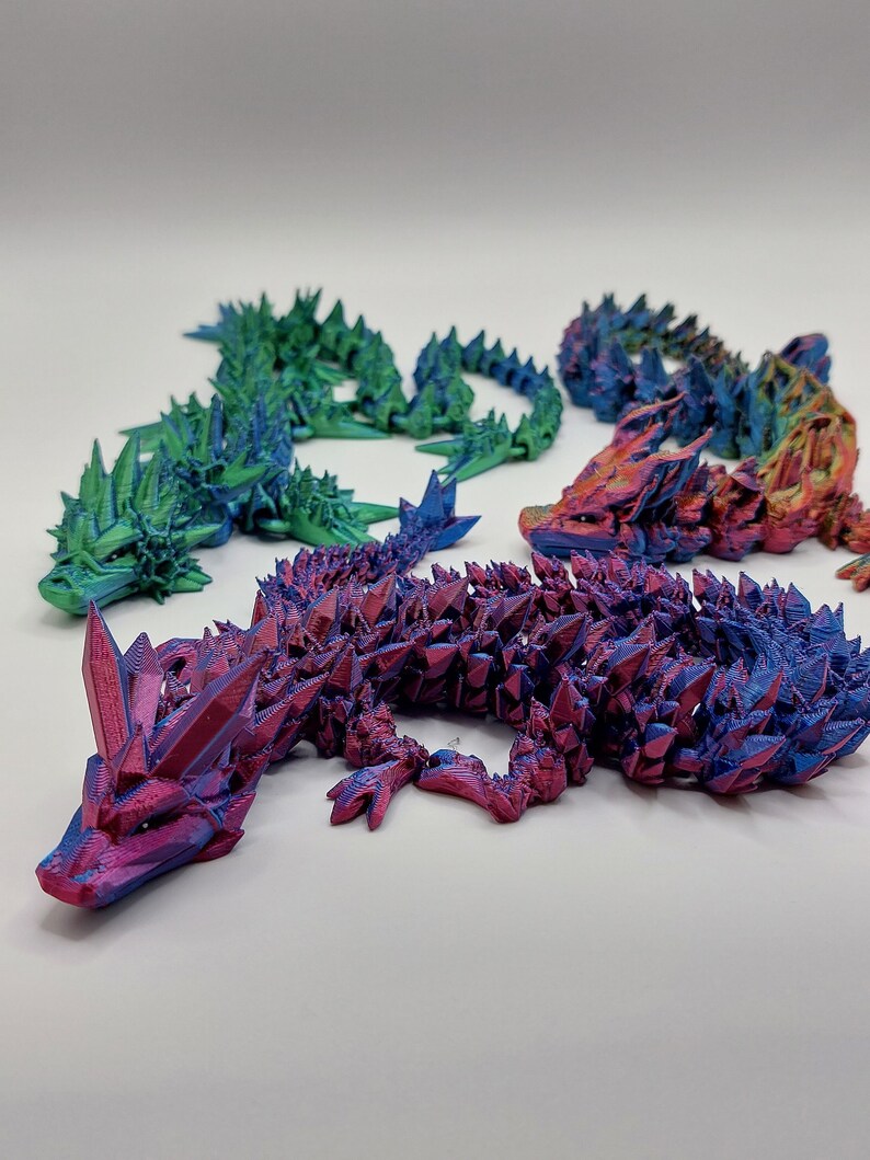 May include: Four 3D printed lizards in different iridescent colors: green, blue, red, and orange. The lizards are posed in a crawling position with their tails curled up.