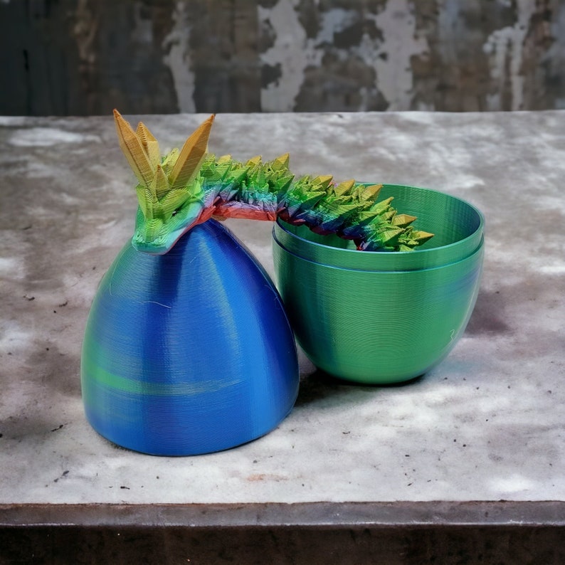 May include: A rainbow iridescent dragon figurine with a green iridescent egg-shaped container. The dragon is curled around the egg.