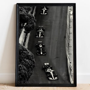 May include: Black and white photograph of five race cars driving on a winding road. The cars are in a line, with the lead car at the top of the image and the last car at the bottom. The road is surrounded by trees and a barrier.