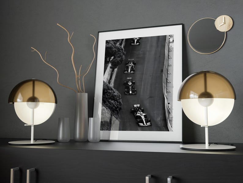May include: Two brown and white glass table lamps with a white base and a black and white photo of race cars on a track in a black frame on a dark gray surface.