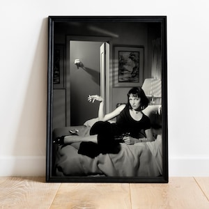 Pode incluir: Impressão emoldurada em preto e branco com uma mulher em um vestido preto reclinada em uma cama, segurando um cigarro e uma arma. A imagem é uma foto de um filme, com uma mão saindo de uma porta ao fundo.
