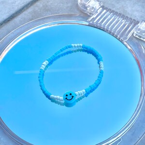 May include: A blue and white beaded bracelet with a blue smiley face charm.