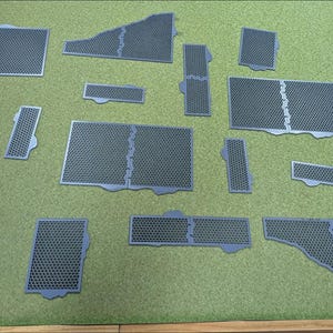 May include: A collection of dark gray modular terrain tiles featuring a consistent hexagonal grid pattern. These flat, geometric pieces vary in size and shape, including rectangular, square, and irregular forms, designed to interlock together.