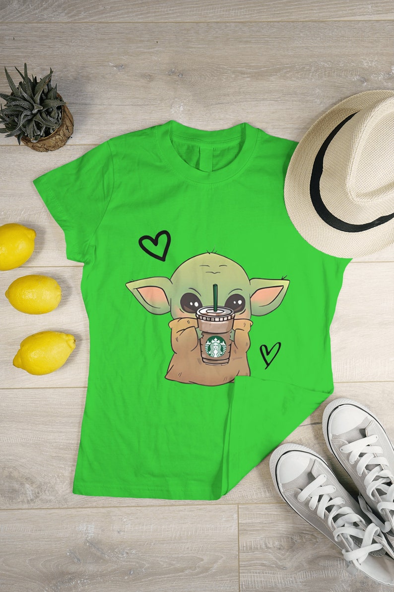 Puede incluir: Camiseta verde con una imagen de dibujos animados de un extraterrestre verde sosteniendo una taza de caf&eacute; con el logotipo de Starbucks. El extraterrestre tiene ojos grandes y est&aacute; rodeado de corazones.