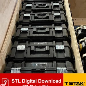 Op de afbeelding: Een stapel zwarte gereedschapskisten met zilveren sluitingen en handvatten, met het label "T STAK" en "STL Digital Download 3D Print File". De gereedschapskisten zijn netjes gerangschikt in een houten container.