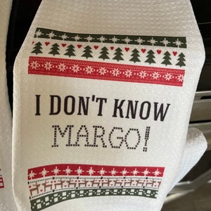 May include: White kitchen towel with a red and green Christmas-themed border and the text "I don't know Margo!" printed in black.