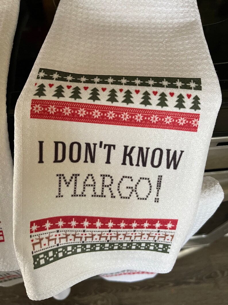 May include: White kitchen towel with a red and green Christmas-themed border and the text "I don't know Margo!" printed in black.