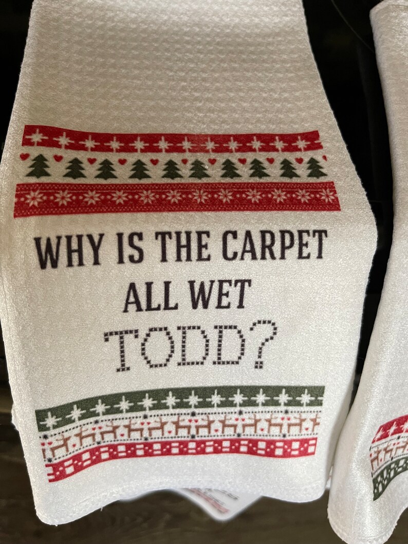 May include: White kitchen towel with a red and green Christmas-themed design. The text "WHY IS THE CARPET ALL WET TODD?" is printed in black.