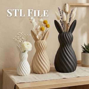 Puede incluir: Tres jarrones con forma de conejo en blanco, beige y negro, cada uno con un diseño en espiral. Los jarrones contienen flores secas y vegetación. El texto "STL FILE" está en la parte superior. Los jarrones están sobre una superficie de madera.