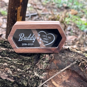 May include: A wooden pet memorial box with a black glass front. The name "Buddy" and dates "2018-2025" are displayed in white script. The right side has a heart with the words "Until We Meet Again".