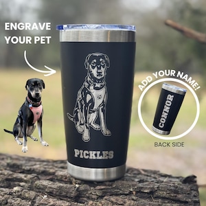 May include: Black stainless steel tumbler with a silver rim and lid. The tumbler features an engraved image of a dog and the name "Pickles" below. The text "Engrave Your Pet" is above the dog image. A smaller tumbler shows the name "Connor".