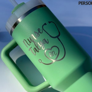 May include: A green travel mug with a handle and a lid. The mug is engraved with the text "Nurse Talya RN" and a stethoscope with a heart.