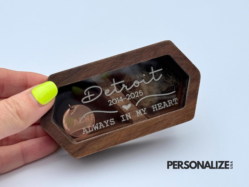 May include: A wooden keepsake box with a clear window, featuring the engraved word "Detroit" and the years 2014-2025. The text "ALWAYS IN MY HEART" is also visible. A small, round copper-colored charm is inside.