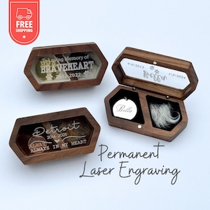May include: Three hexagonal dark wood keepsake boxes with clear lids. Two boxes are closed, displaying engraved text including "In loving memory of BRAVEHEART 2012-2022" and "Detroit 2014-2025 ALWAYS IN MY HEART". One open box contains a silver disc and fur.