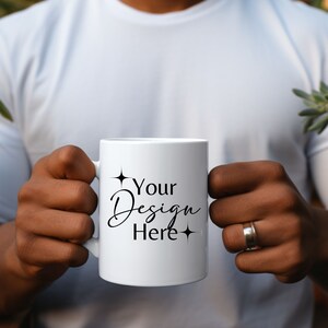Può includere: Una tazza di ceramica bianca con la scritta "Your Design Here" in corsivo nero. La tazza è tenuta da una persona che indossa una maglietta bianca. Il design è affiancato da due stelle nere.