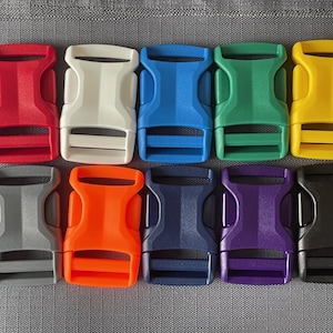 May include: Ten plastic buckle closures in various colors, including red, white, blue, green, yellow, gray, orange, navy, purple, and black. The buckles are all the same size and shape, and they have a smooth, matte finish.