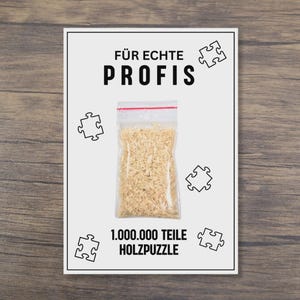Könnte beinhalten: Eine weiße Karte mit dem Text "FÜR ECHTE PROFIS" und "1.000.000 TEILE HOLZPUZZLE". Sie zeigt einen transparenten Plastikbeutel gefüllt mit Puzzleteilen und Puzzleteil-Umrissen.