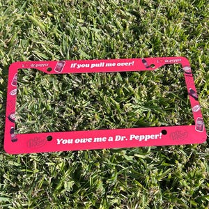 Può includere: Cornice rossa per targa con la scritta "If you pull me over!" e "You owe me a Dr. Pepper!" in bianco. La cornice presenta loghi Dr. Pepper e la scritta "I ❤️ dr.pepper".