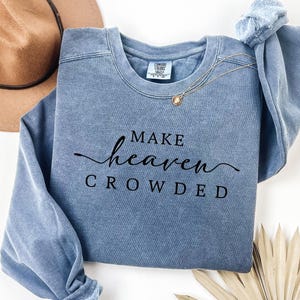 May include: A blue sweatshirt with the text "Make heaven crowded" in black lettering.