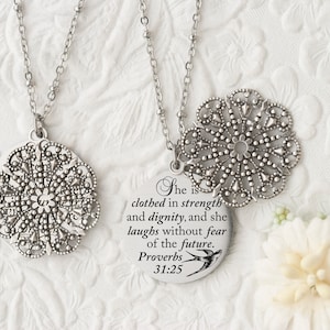 May include: Two silver-toned necklaces with intricate, openwork floral pendants. One pendant is round with the text "She is clothed in strength and dignity, and she laughs without fear of the future. Proverbs 31:25".