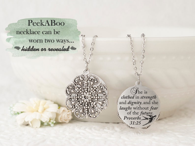 May include: A silver-toned necklace with a detailed, openwork pendant and a delicate chain. The necklace can be worn two ways, as the image text indicates. The second pendant has an inscription from Proverbs 31:25 and a small bird illustration.