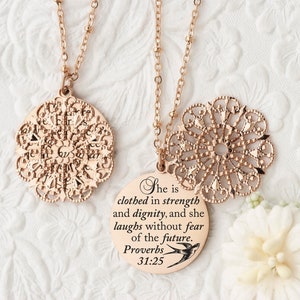 May include: Rose gold necklaces with intricate filigree pendants. One necklace features a round pendant with the text "She is clothed in strength and dignity, and she laughs without fear of the future. Proverbs 31:25" and a small bird.