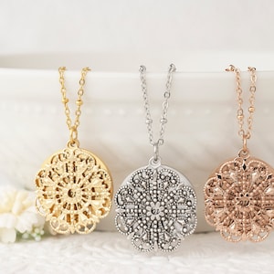May include: Three filigree pendant necklaces in gold, silver, and rose gold. Each necklace features a detailed, circular pendant suspended from a delicate chain. The pendants have an openwork design with intricate patterns, showcasing a vintage or bohemian style.