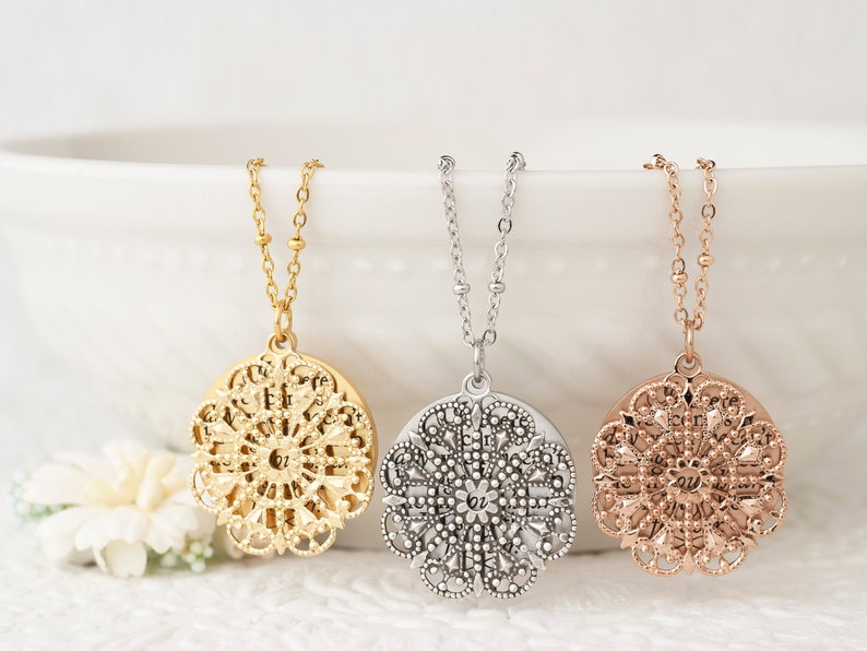 May include: Three filigree pendant necklaces in gold, silver, and rose gold. Each necklace features a detailed, circular pendant suspended from a delicate chain. The pendants have an openwork design with intricate patterns, showcasing a vintage or bohemian style.