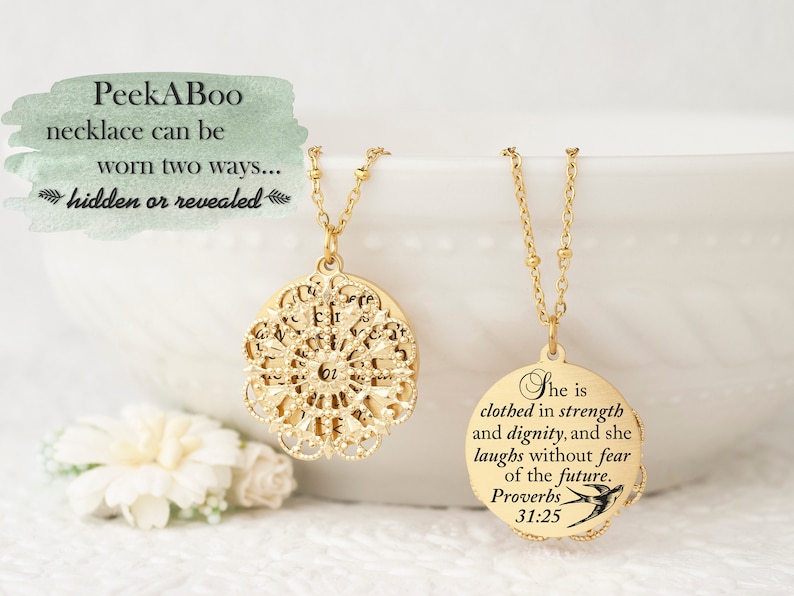 May include: Two gold-colored necklaces with pendant designs. One pendant is a filigree design, and the other is a round pendant with the text "She is clothed in strength and dignity, and she laughs without fear of the future. Proverbs 31:25". The text "PeekABoo necklace can be worn two ways... hidden or revealed" is also present.