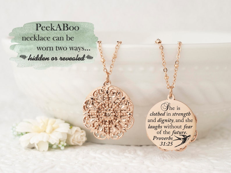 May include: A rose gold PeekABoo necklace with a filigree pendant and a round pendant with the text "She is clothed in strength and dignity, and she laughs without fear of the future. Proverbs 31:25". The necklace can be worn two ways: hidden or revealed.