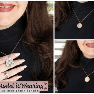 May include: A silver-toned necklace with an intricate, circular pendant is displayed. The pendant has a detailed, openwork design. The necklace is shown on a person wearing a black turtleneck. The text "Model is Wearing" and "18 inch chain length" is visible.