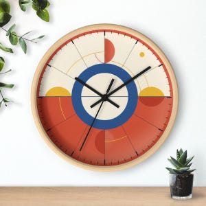 Peut inclure: Une horloge murale ronde avec un cadre en bois clair et un cadran crème et rouge terre cuite. Le design présente un cercle bleu central, des aiguilles noires et des formes géométriques incluant des demi-cercles jaunes et rouges.