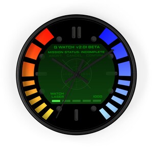 Puede incluir: Un reloj negro y verde con una pantalla digital que dice "Q WATCH V2.01 BETA MISSION STATUS: INCOMPLETE ABORT CANCEL CONFIRM WATCH LASER 1000". El reloj tiene una barra roja y naranja a la izquierda y una barra azul a la derecha.