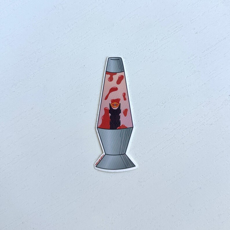 May include: A red and white lava lamp with a black silhouette of a creature with an eye inside. The lava lamp is on a white background.