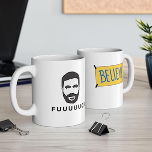 Könnte beinhalten: Zwei weiße Keramikbecher mit unterschiedlichen Designs. Ein Becher zeigt eine Schwarzweißillustration eines Männergesichts mit Bart und dem Text "FUUUUUCK". Der andere Becher zeigt ein gelbes Banner mit dem Text "BELIEVE" in blauen Buchstaben.