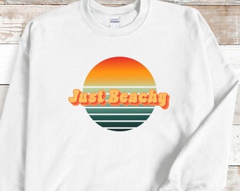 May include: White sweatshirt with a retro sunset graphic and the text "Just Beachy" in orange.