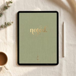Puede incluir: Una tableta verde salvia con la palabra "noted" en letras doradas. Un lápiz óptico blanco descansa junto a la tableta. Una taza de café y una ramita de vegetación también están en la imagen. La tableta tiene un borde negro.