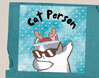 May include: A white cat wearing sunglasses and a headband with reindeer antlers. The cat is doing a dabbing dance pose. The background is a blue pattern with white and orange cat faces. The text "Cat Person" is written in black at the top of the image.