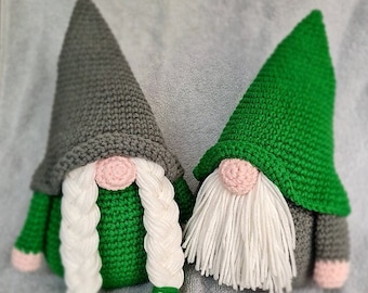 May include: Two crocheted gnomes, one with a gray hat and the other with a green hat. Both gnomes have white yarn beards and pink faces.