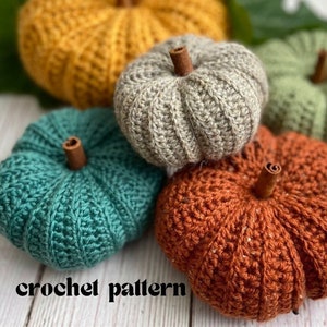 Puede incluir: Cuatro calabazas de ganchillo en diferentes colores: naranja, verde, gris y verde azulado. Las calabazas están dispuestas sobre una superficie de madera blanca con una hoja verde en el fondo. El texto "crochet pattern" es visible en la parte inferior de la imagen.