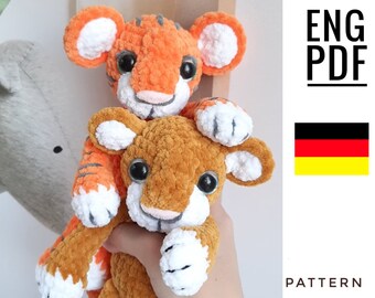 May include: Two crocheted tiger plushies, one orange and one brown, with white accents. The orange tiger is holding the brown tiger in its paws. The image includes the text "ENG PDF PATTERN".