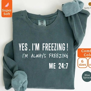 Może przedstawiać: Niebiesko-zielona bluza z białym napisem "YES. I'M FREEZING! I'M ALWAYS FREEZING ME 24:7". Bluza ma okrągły dekolt i długie rękawy. Obraz zawiera również słowa "Super Soft", "Comfort Colors" i "Blue Spruce".