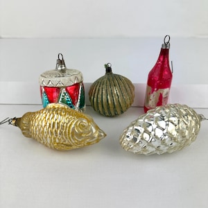 May include: A collection of vintage Christmas ornaments. Includes a gold fish, a red and silver drum, a green and gold onion-shaped ornament, a red bottle, and a silver pinecone.