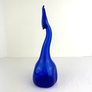 May include: A tall, cobalt blue glass vase with a rounded base and a long, slender, curved neck that tapers upward. The glass features a smooth, translucent finish with subtle variations in color intensity throughout the elongated structure.